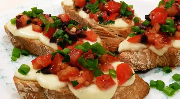 Bruschetta z pomidorami i mozzarellą: chrupiące grzanki z roztopionym serem, świeżymi pomidorami, oliwkami i szczypiorkiem. Idealny przepis na szybką przekąskę.