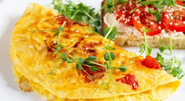 Złocisty omlet z pomidorami, posypany sezamem, podany z tostami i kiełkami. Pyszne śniadanie.