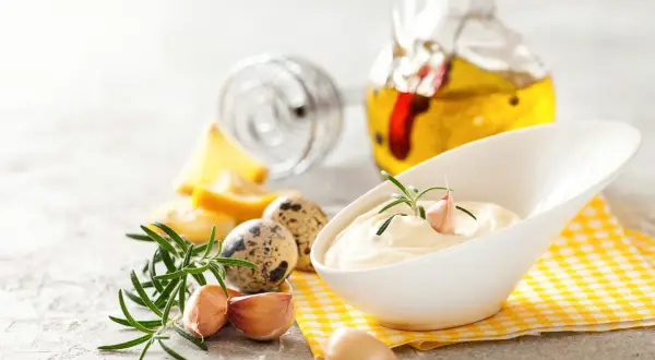 Kremowy sos aioli z czosnkiem i rozmarynem, obok jaj przepiórczych i butelki oliwy.