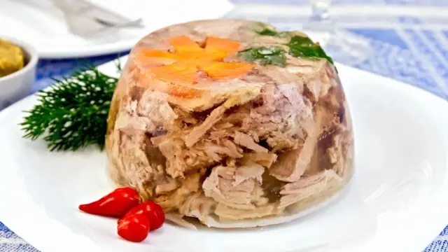 Pyszny auszpik z mięsem, marchewką i natką pietruszki, ozdobiony koperkiem i papryczkami chili.