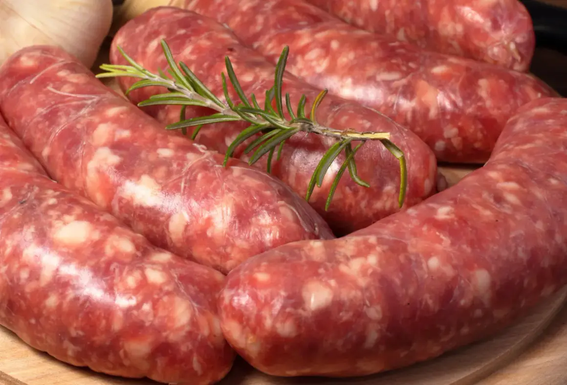Świeża salsiccia z gałązką rozmarynu i czosnkiem w tle, gotowa do grillowania.