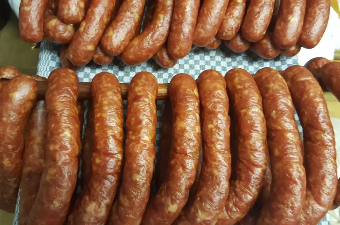 Gotowy przepis na kiełbasę swojską 5 kg. Wędliny wiszą na drewnianych kijach, gotowe do dalszej obróbki.