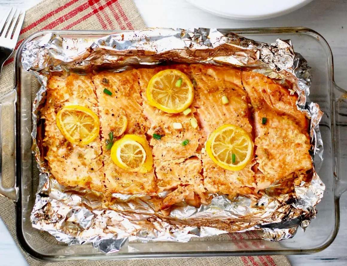 Pyszny, pieczony filet z łososia z plasterkami cytryny i szczypiorkiem, podany w folii aluminiowej.