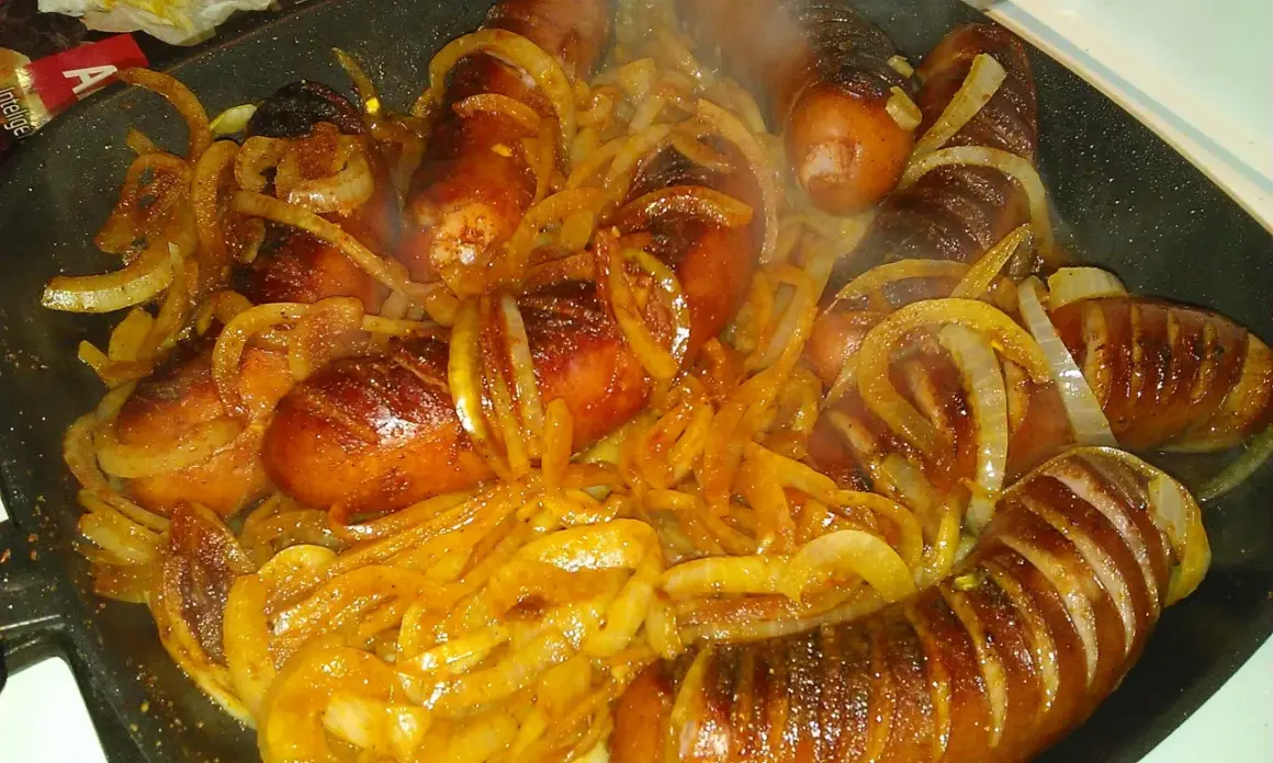 Gorąca, rumiana kiełbasa z cebulą dusi się na patelni, tworząc apetyczny aromat.