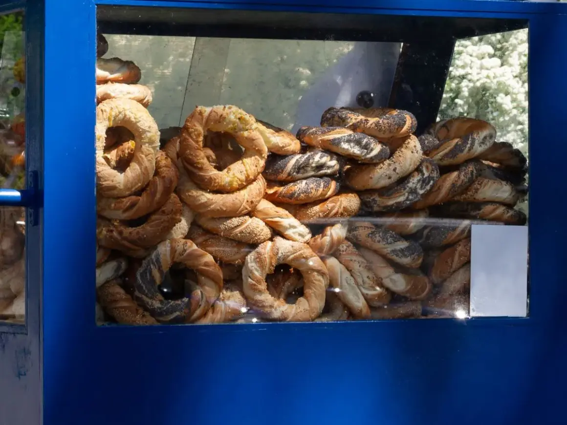 Stos świeżych obwarzanków w niebieskiej budce. Widać obwarzanki z makiem, sezamem i posypką serową.