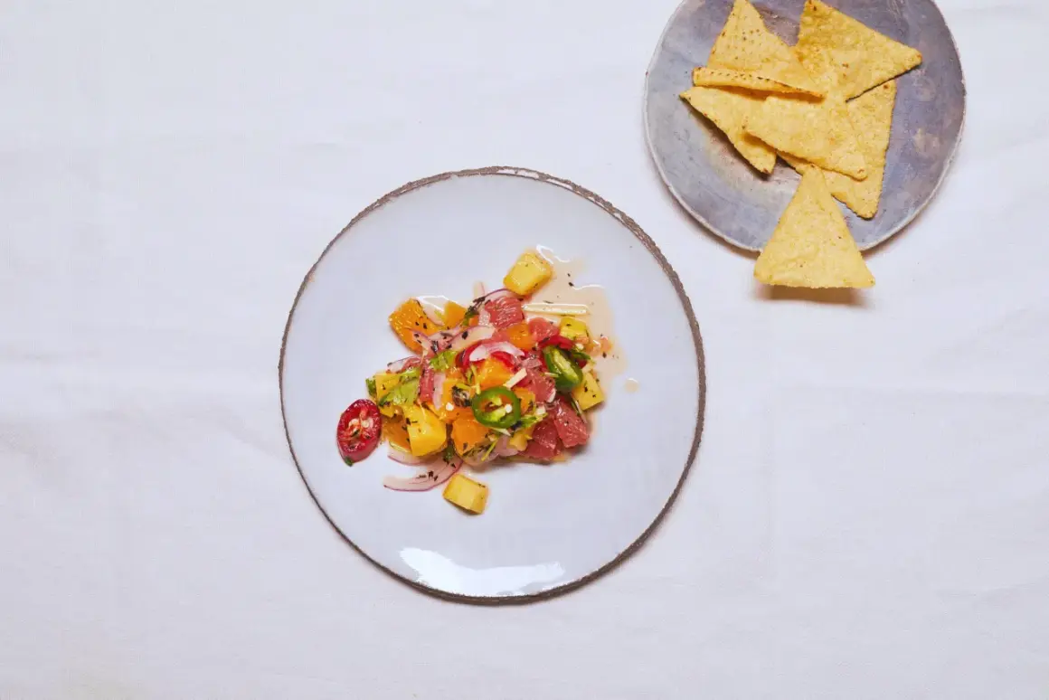 Kolorowe ceviche z owocami cytrusowymi, ananasem, papryczką chili i czerwoną cebulą, podane na talerzu obok nachos.