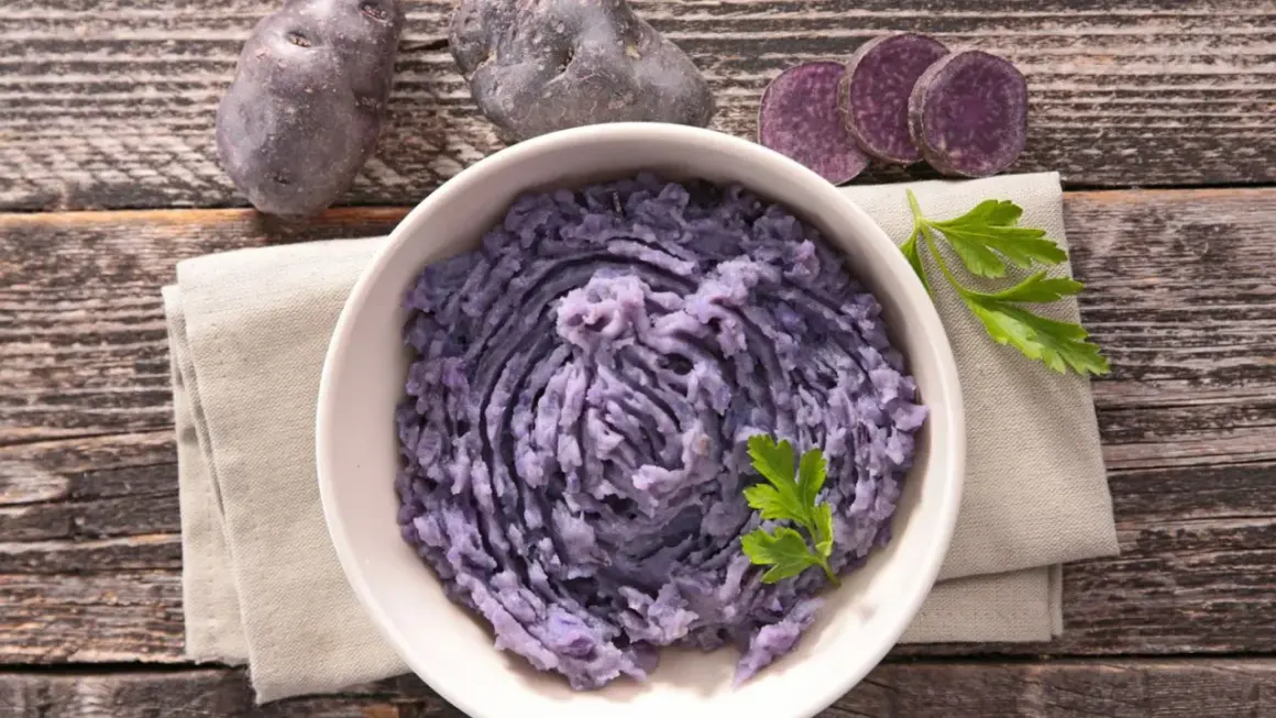 Fioletowe ziemniaki w misce, obok kilka sztuk i plasterki. Pyszne purée z fioletowych ziemniaków.