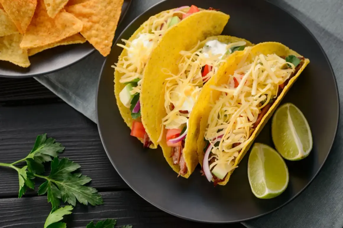 Pyszne tacos z kurczakiem, z serem, warzywami i limonką. Obok nachos i natka pietruszki.