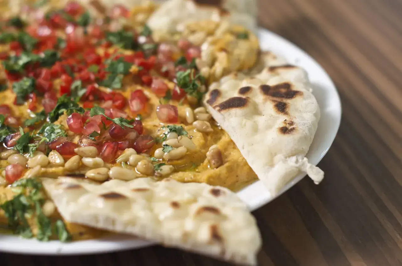 Chlebek naan z czym podawać? Pyszny hummus z granatem, orzeszkami pinii i natką pietruszki, idealny do maczania.