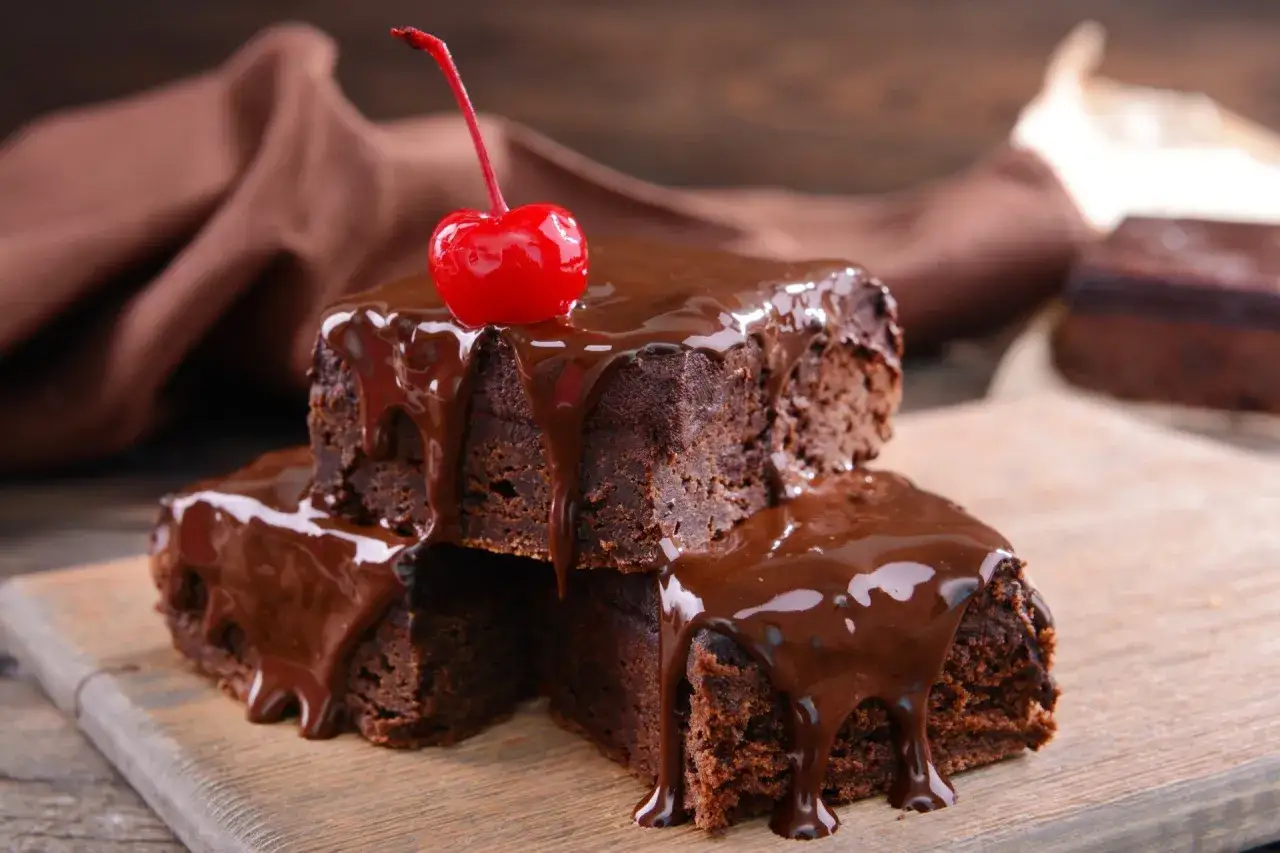 Słodkie brownie z polewą czekoladową z czekolady i mleka, ozdobione wiśnią.