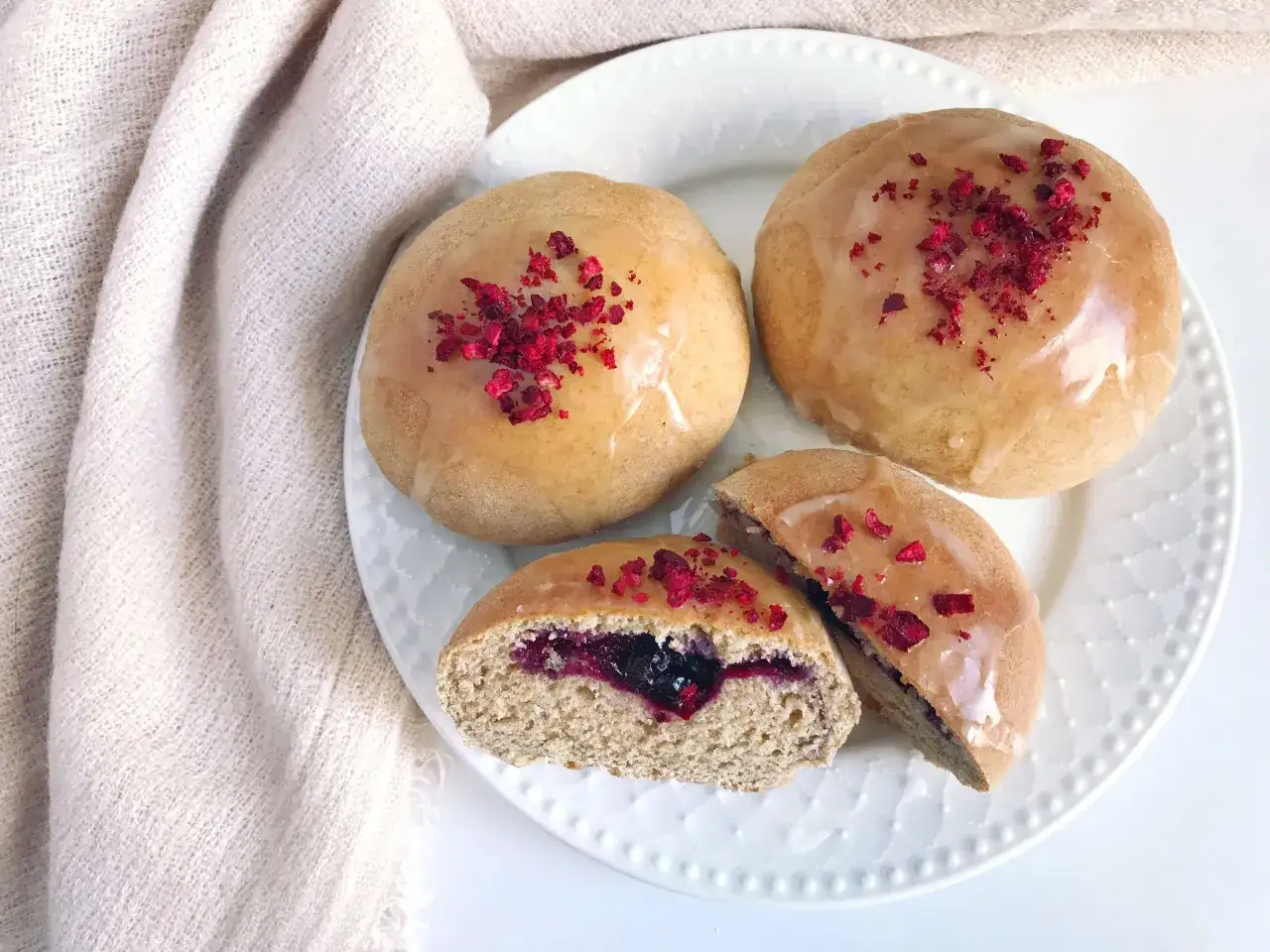 Szybkie pączki z piekarnika z jagodowym nadzieniem, lukrem i liofilizowanymi malinami.