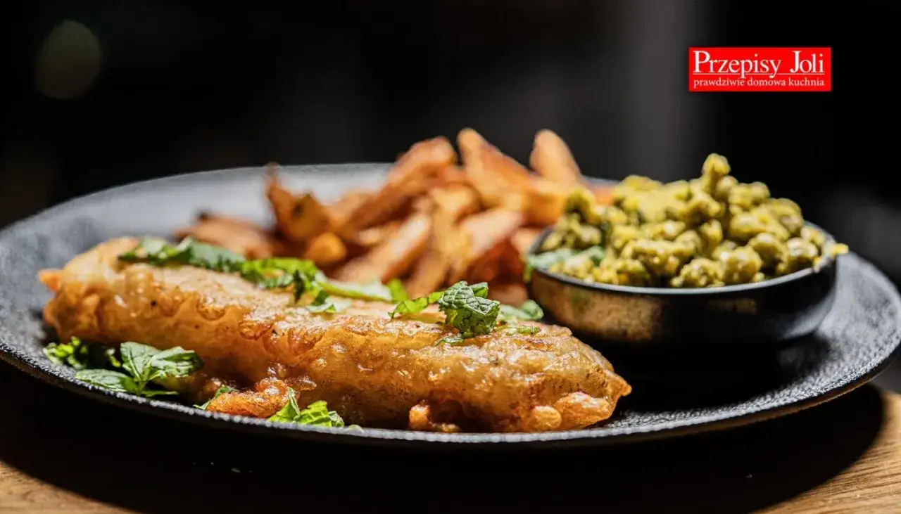 Chrupiące fish and chips z groszkiem na talerzu.