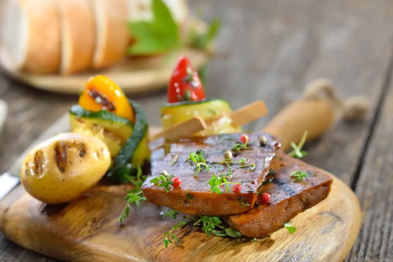 Grillowany seitan co to? Plasterki seitanu z ziołami i pieprzem, podane z pieczonymi ziemniakami i szaszłykami z warzyw.