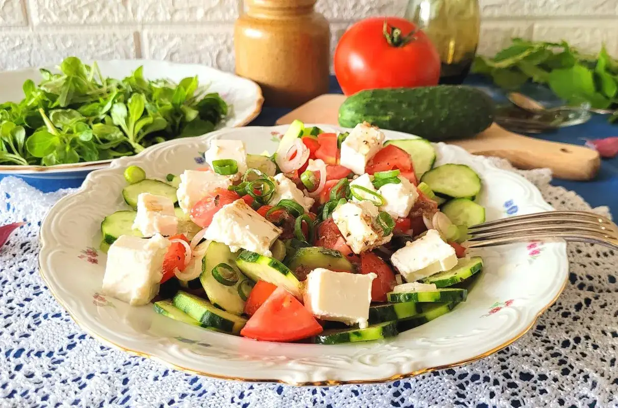 Pyszna sałatka z serem feta, pomidorem i ogórkiem, posypana szczypiorkiem. Idealna na lekki posiłek.