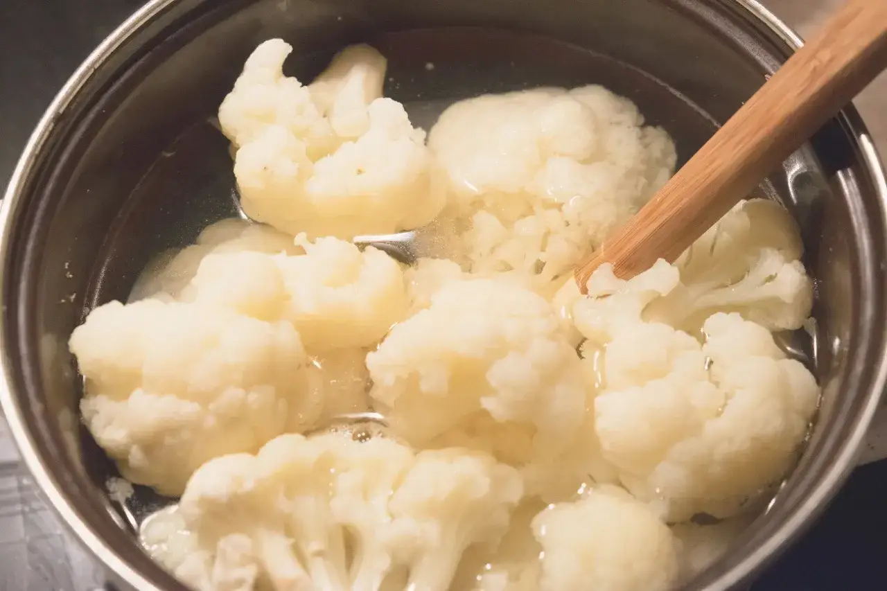 Kalafior gotuje się w garnku. Drewniana łyżka pomaga sprawdzić, jak ugotować kalafior do idealnej miękkości.