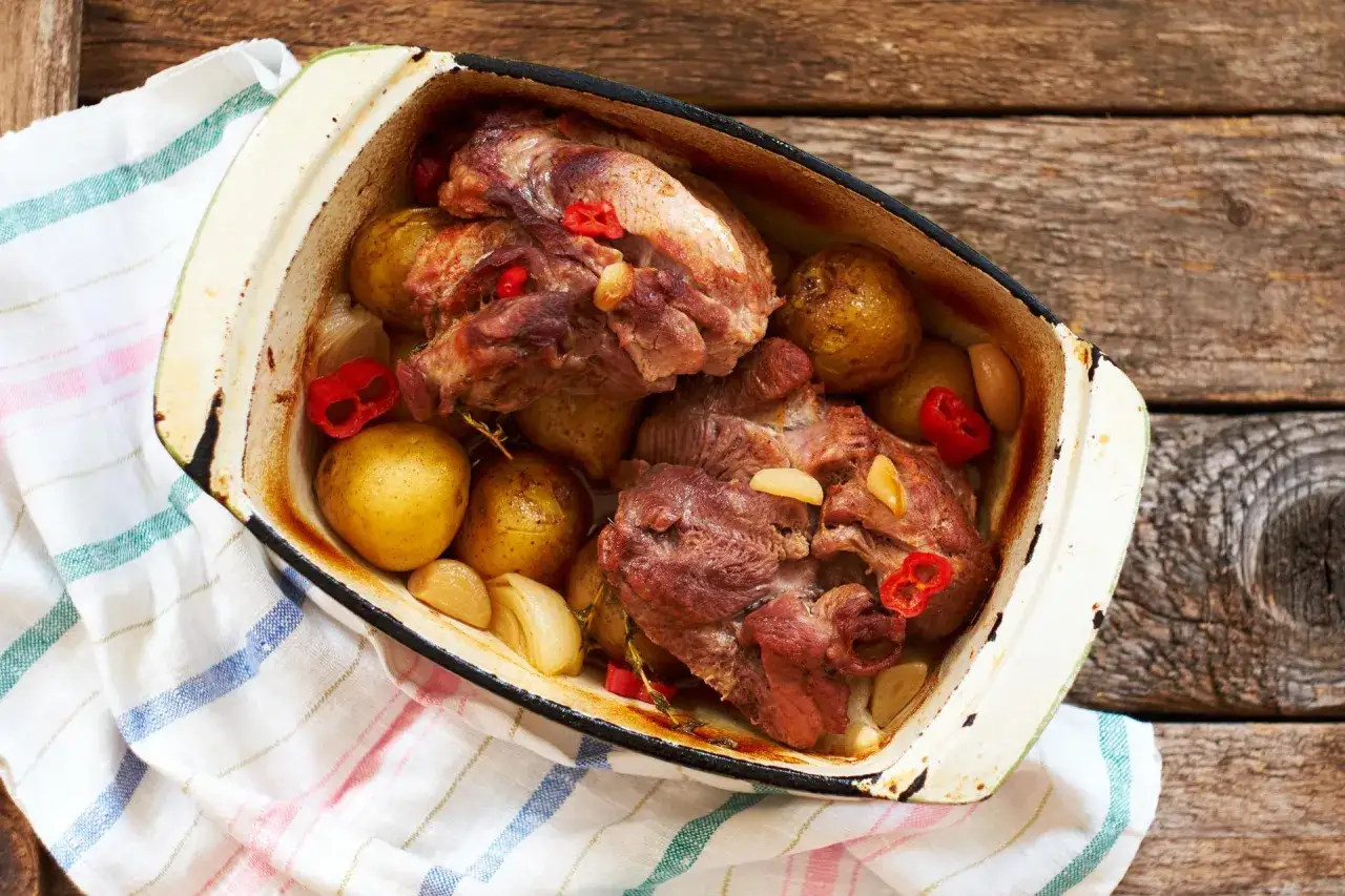Pyszna pieczeń wieprzowa z ziemniakami, czosnkiem i papryczką chili w naczyniu żaroodpornym.