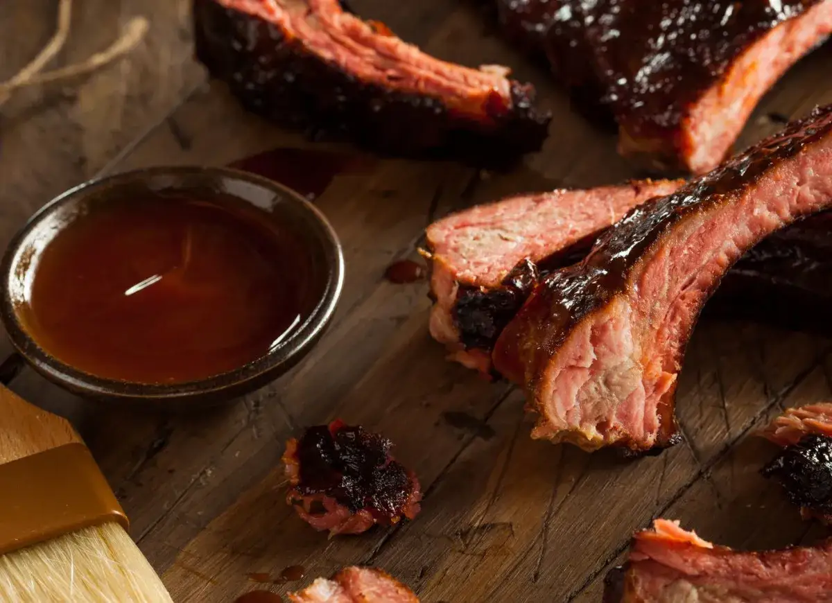 Soczyste żeberka w sosie barbecue, obok miseczka z sosem i pędzelek. Idealna przyprawa do żeberek na drewnianej desce.