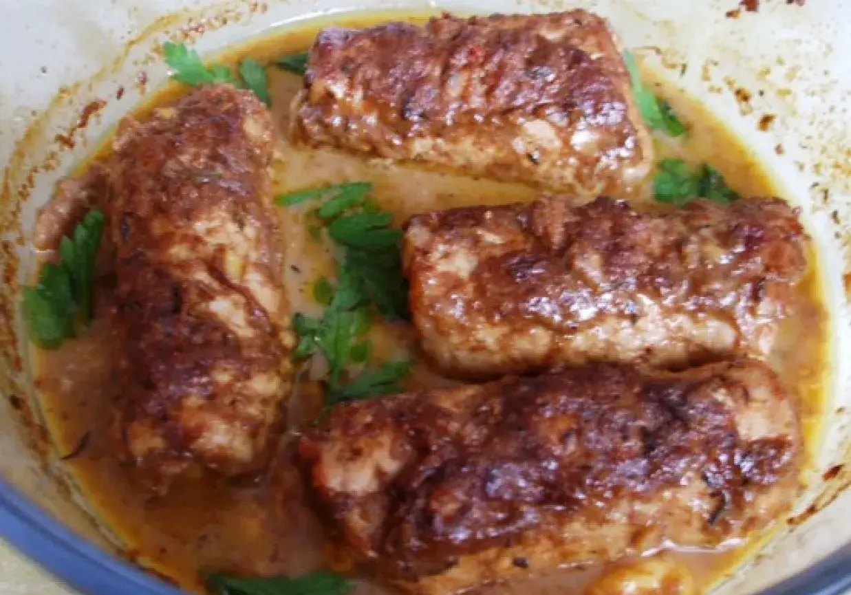 Roladki schabowe pieczone w naczyniu, zanurzone w aromatycznym sosie, ozdobione świeżą natką pietruszki.