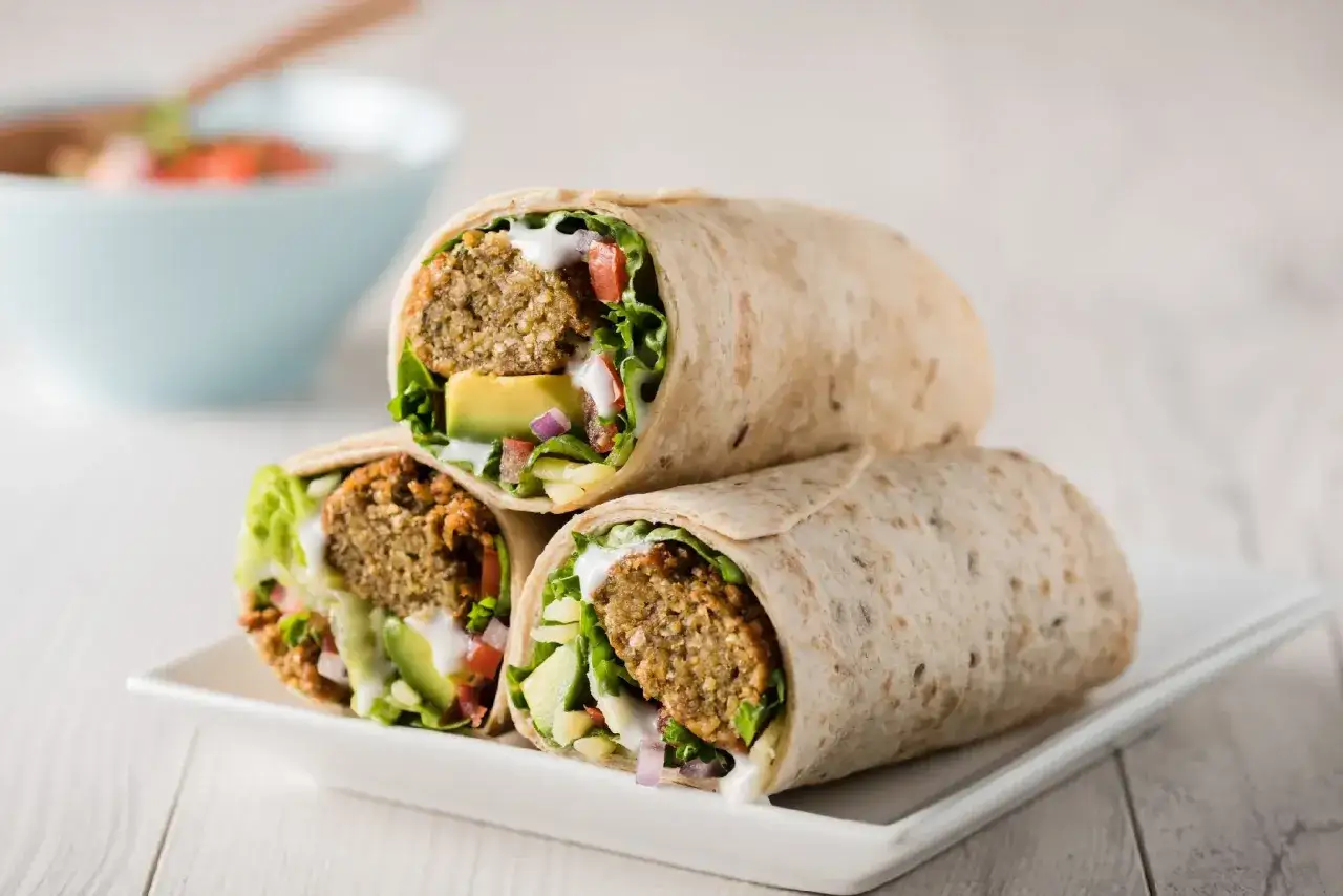 Trzy sycące falafel kebaby z awokado, sałatą i sosem na talerzu.
